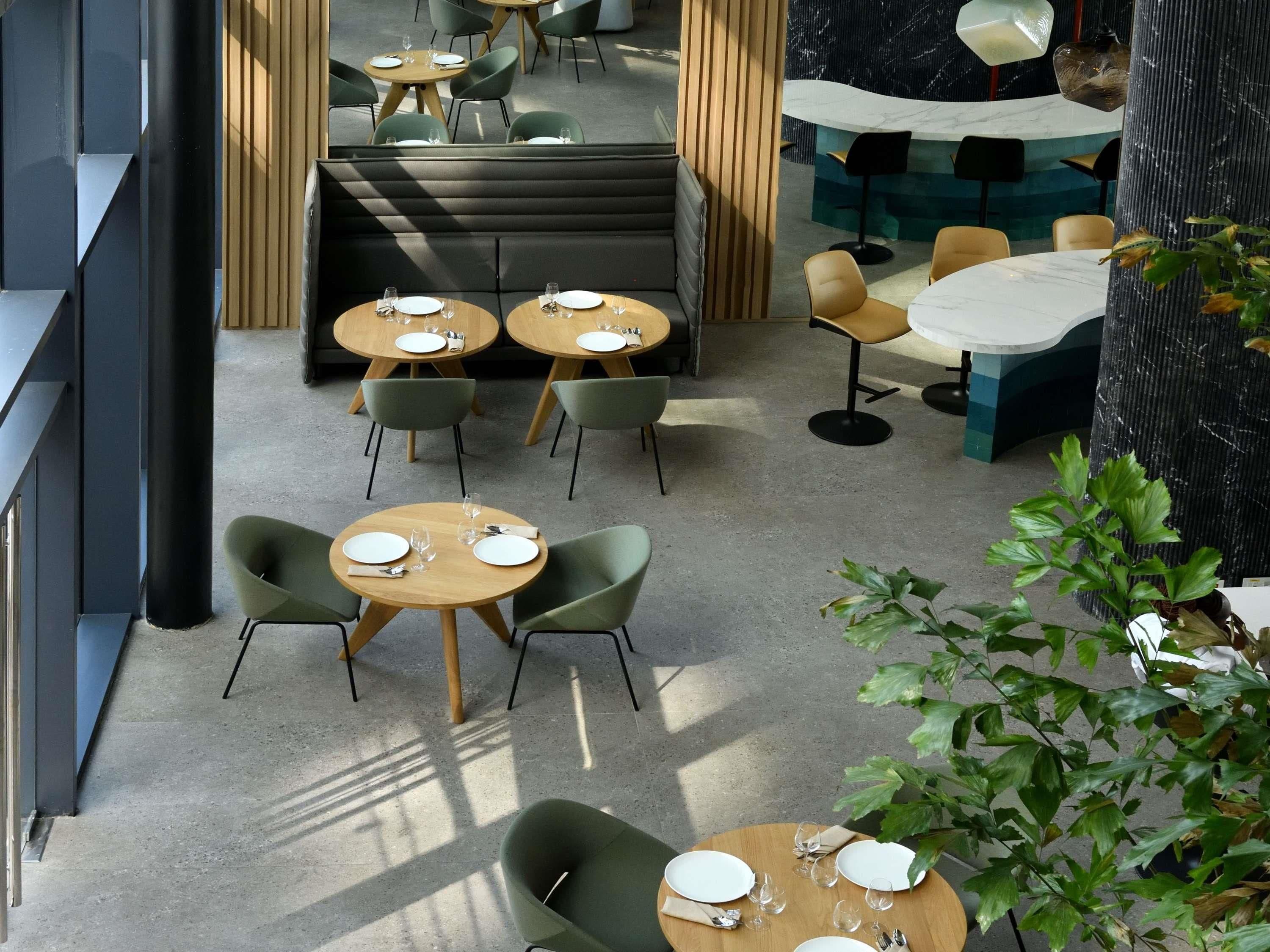 Un comedor moderno con mesas redondas, sillas verdes y una zona de estar con un banco acolchado.
