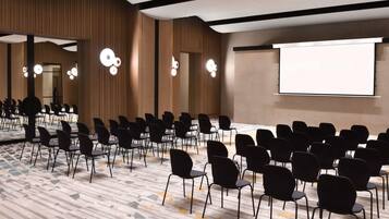 Ein Konferenzraum mit Reihen von Stühlen, einer großen Leinwand und modernen Leuchten.
