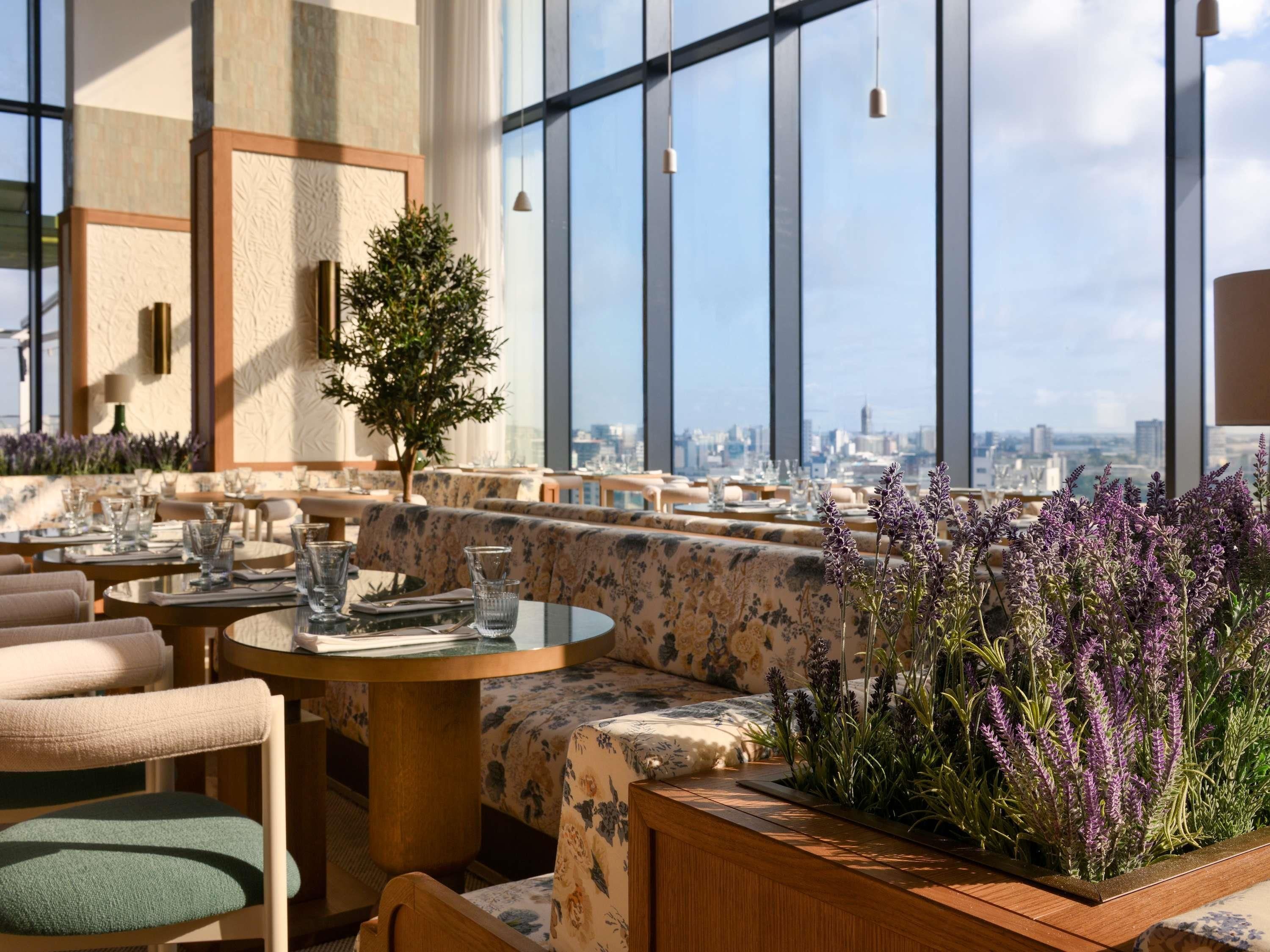 A rooftop restaurant with round tables, cushioned seating, and a view of the city skyline.