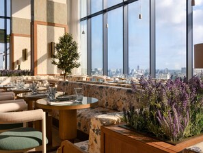 En restaurang på taket med runda bord, bekväma sittplatser och utsikt över stadens silhuett.