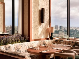 Comedor con mesa preparada para cuatro personas, un sofá y vistas a la ciudad.