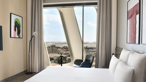 Habitación de hotel con una cama grande, una silla, un escritorio con un florero y vistas a la ciudad.