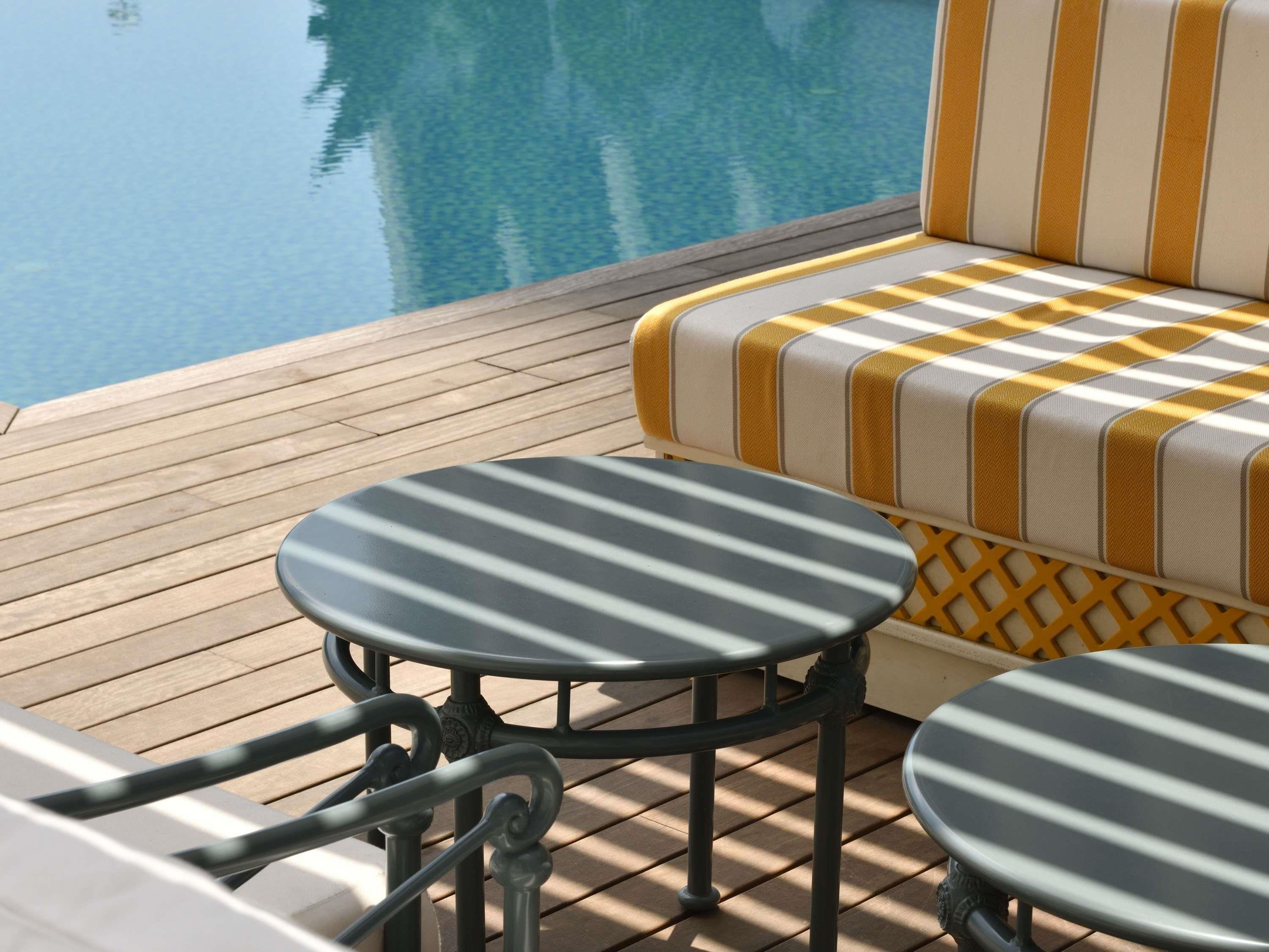 Un espace aménagé près de la piscine, avec un canapé à carreaux et deux tables rondes dont les plateaux sont à rayures.
