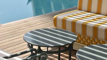 Un espace aménagé près de la piscine, avec un canapé à carreaux et deux tables rondes dont les plateaux sont à rayures.