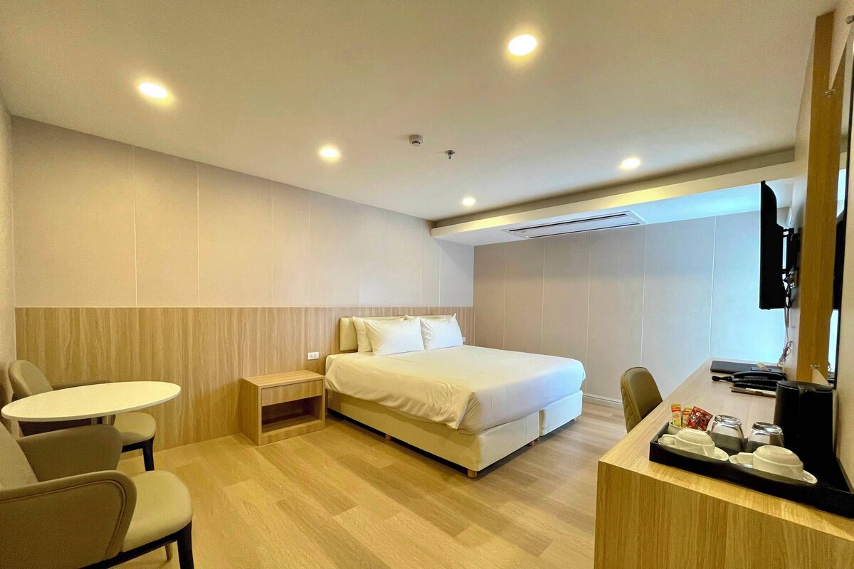 A hotel room with a bed, a desk, a chair, a small table, and a TV.