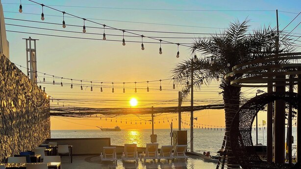 Un patio frente al agua con mesas al aire libre y vistas al atardecer sobre el mar.