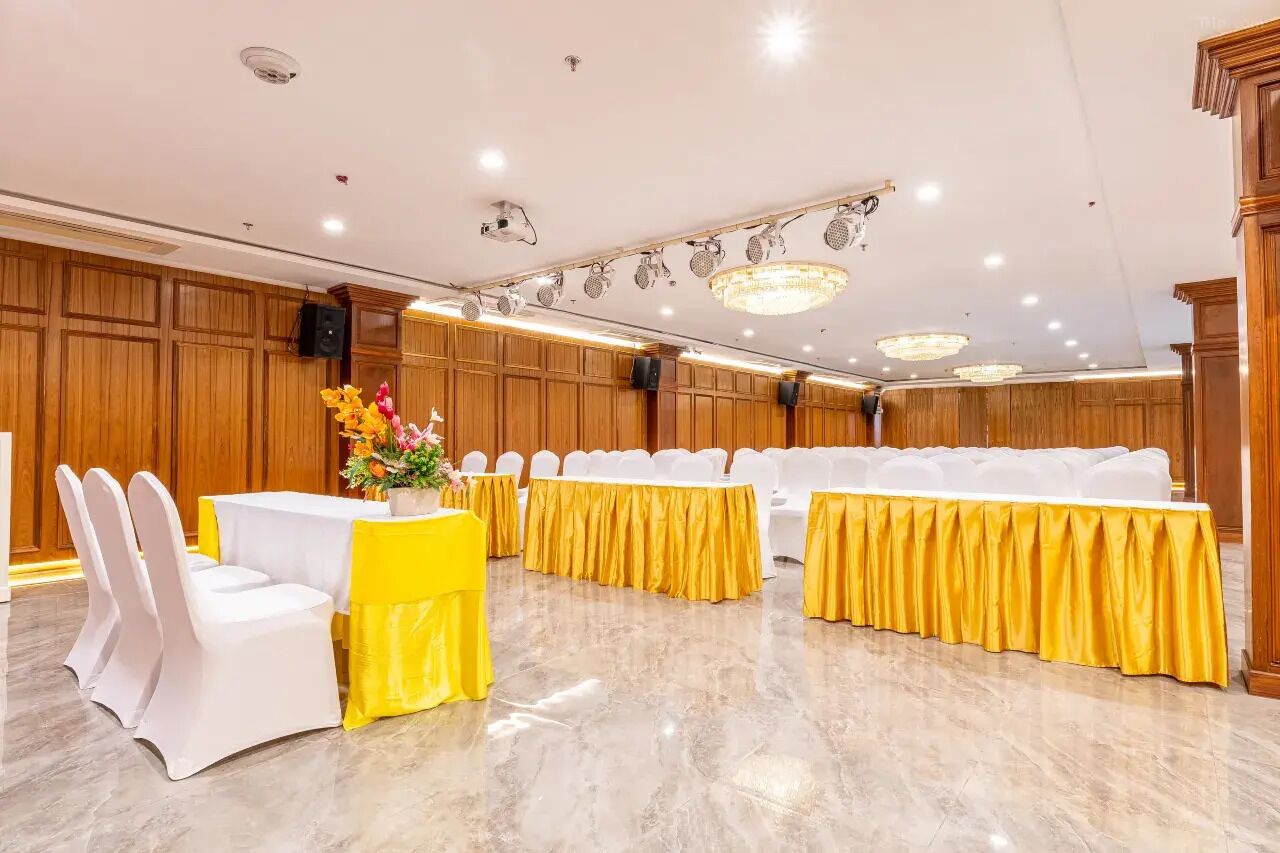 A banquet hall with white chairs and tables, yellow tablecloths, and a chandelier.
