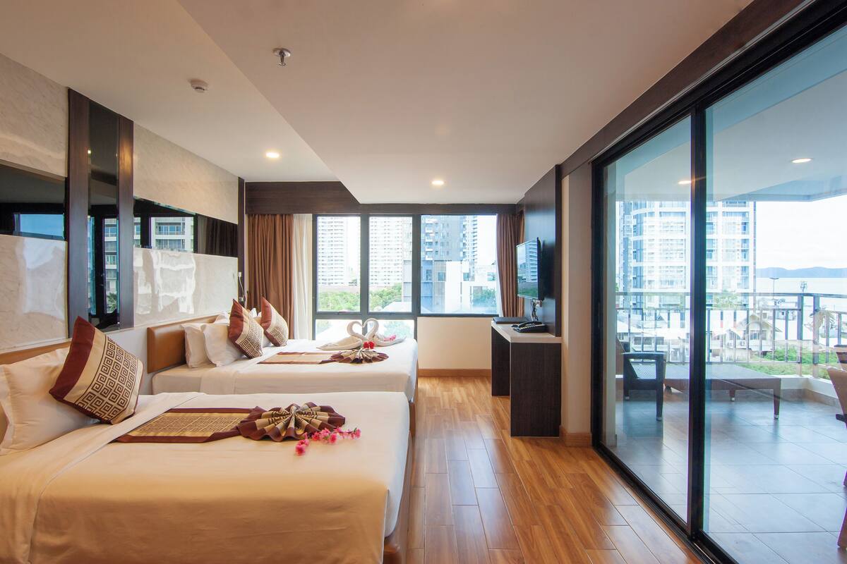 Habitación de hotel con dos camas, un escritorio y un ventanal grande con vista a la ciudad.