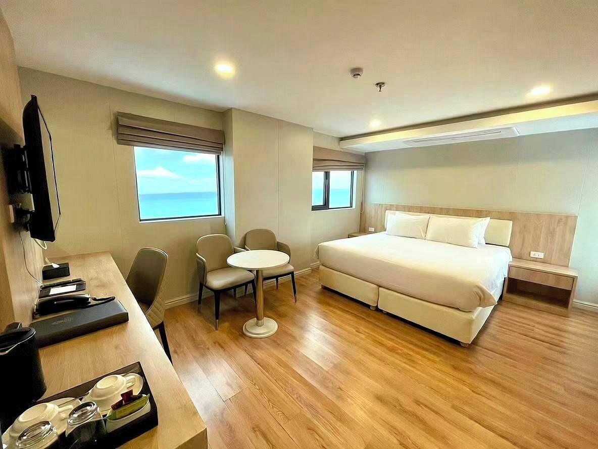 A hotel room with a bed, a desk, a chair, a small table, and a TV.