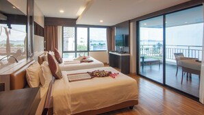 Habitación de hotel con dos camas, un balcón con mesa y sillas, y un televisor sobre un escritorio.