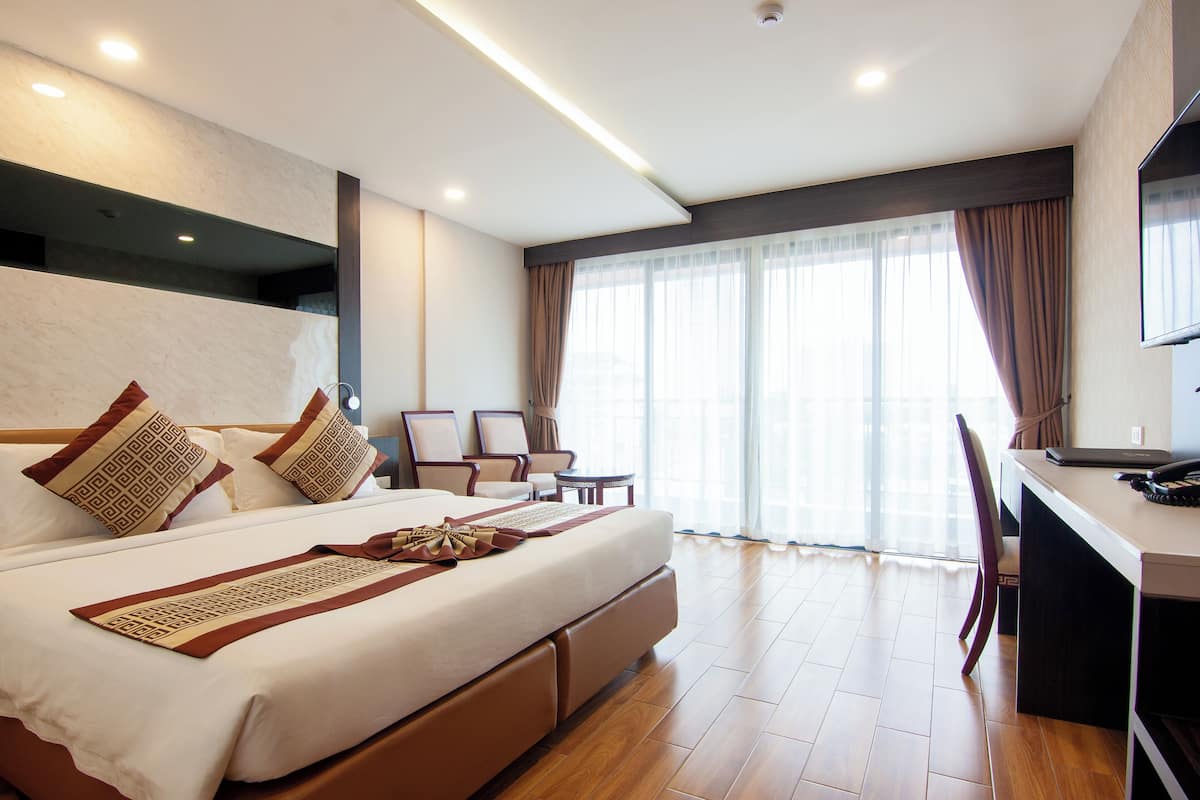 Habitación de hotel moderna con una cama grande, un escritorio y vistas de la ciudad a través de amplios ventanales.