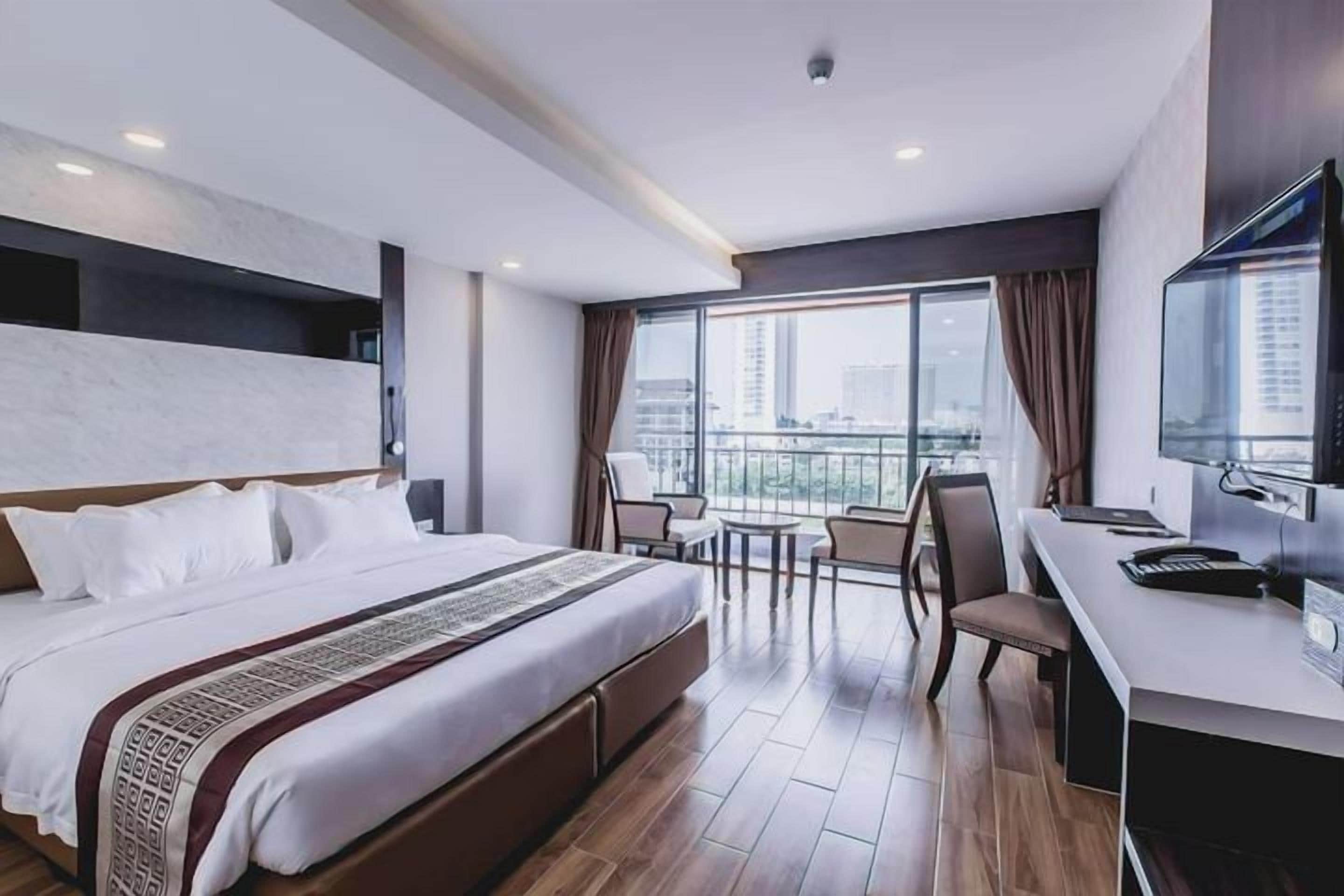 Une chambre d’hôtel avec un grand lit, un bureau avec une chaise, une télévision et un balcon offrant une vue sur la ville.