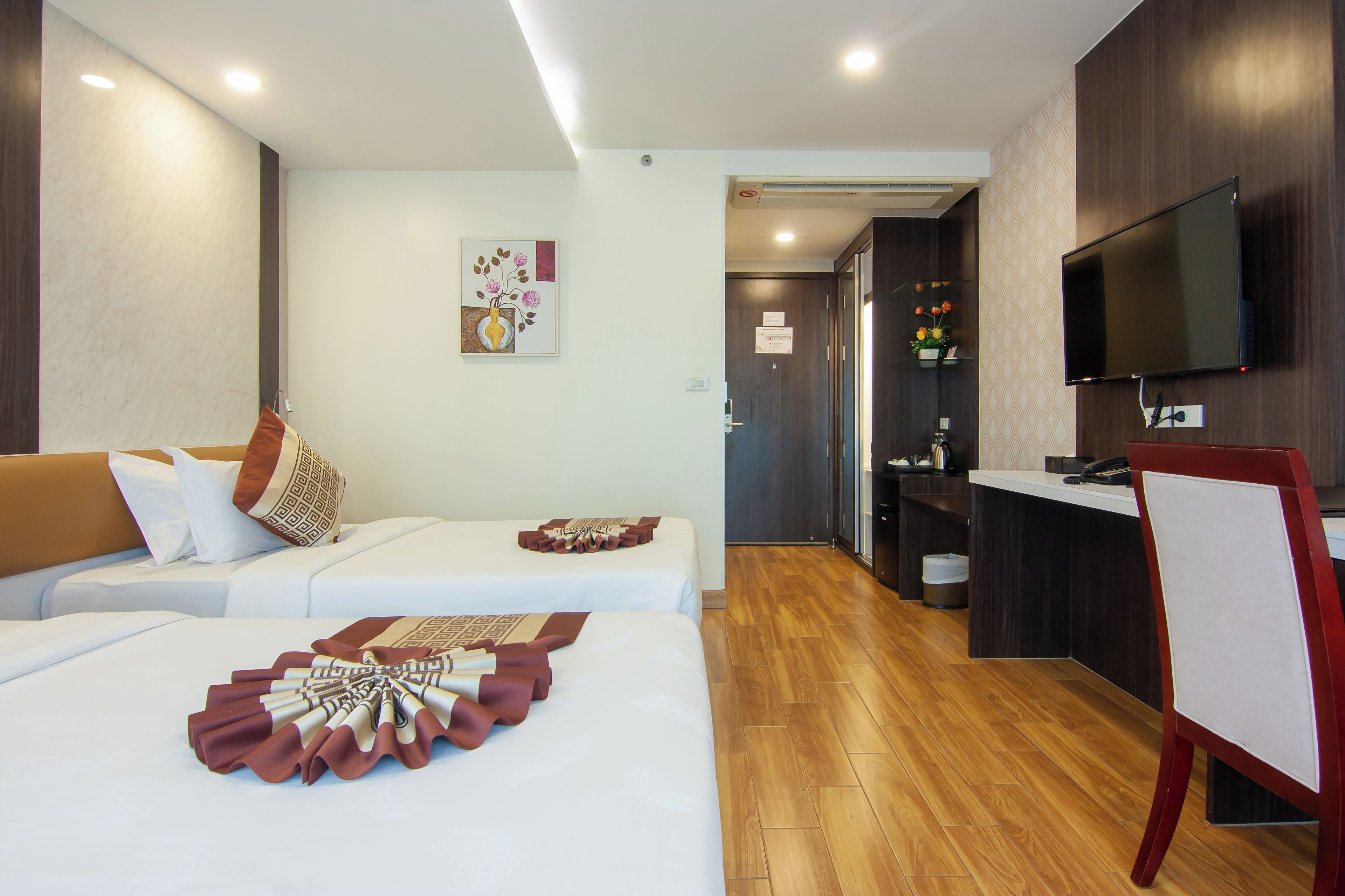 A modern hotel room with a sofa bed, a dining area, and a TV mounted on the wall.