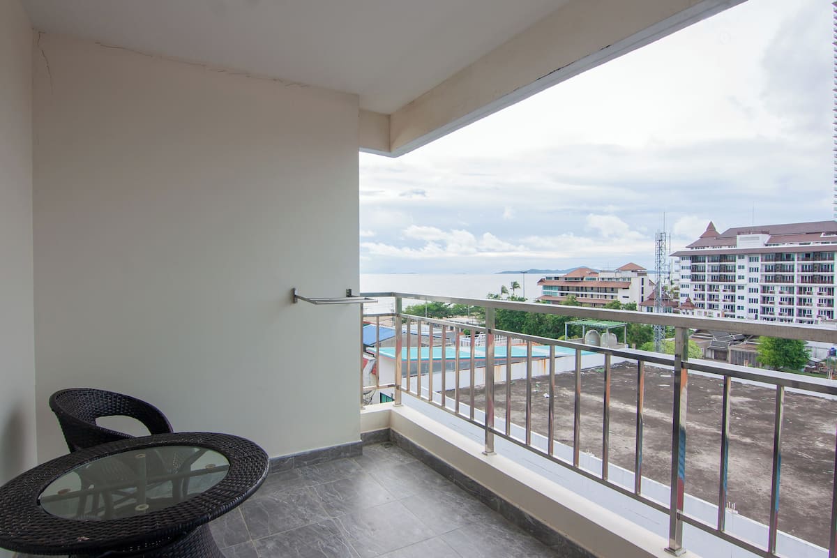 Un balcón con una mesa y sillas de vidrio, con vistas a una piscina y edificios.