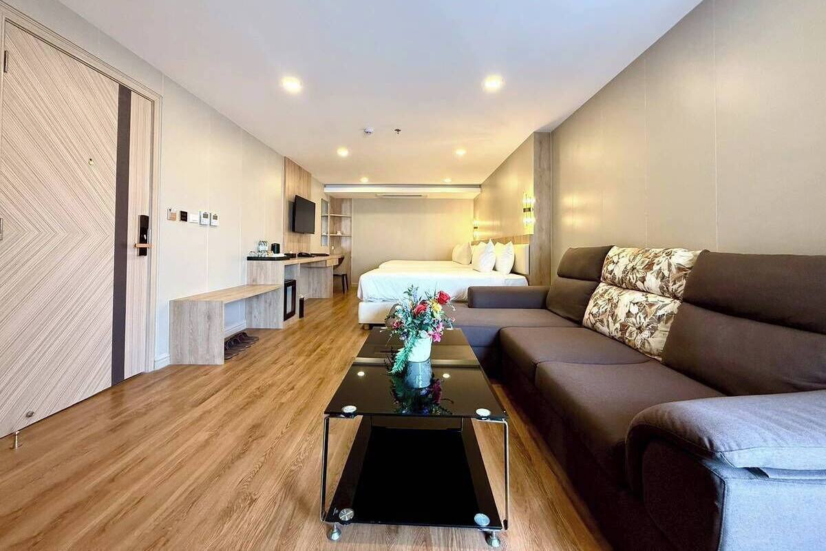 Una habitación de hotel moderna con suelo de madera, un sofá, una mesa de centro con un jarrón, una cama, un escritorio y un televisor.