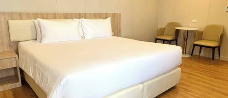 Een moderne hotelkamer met een groot bed, een tafeltje, twee stoelen en een houten vloer.