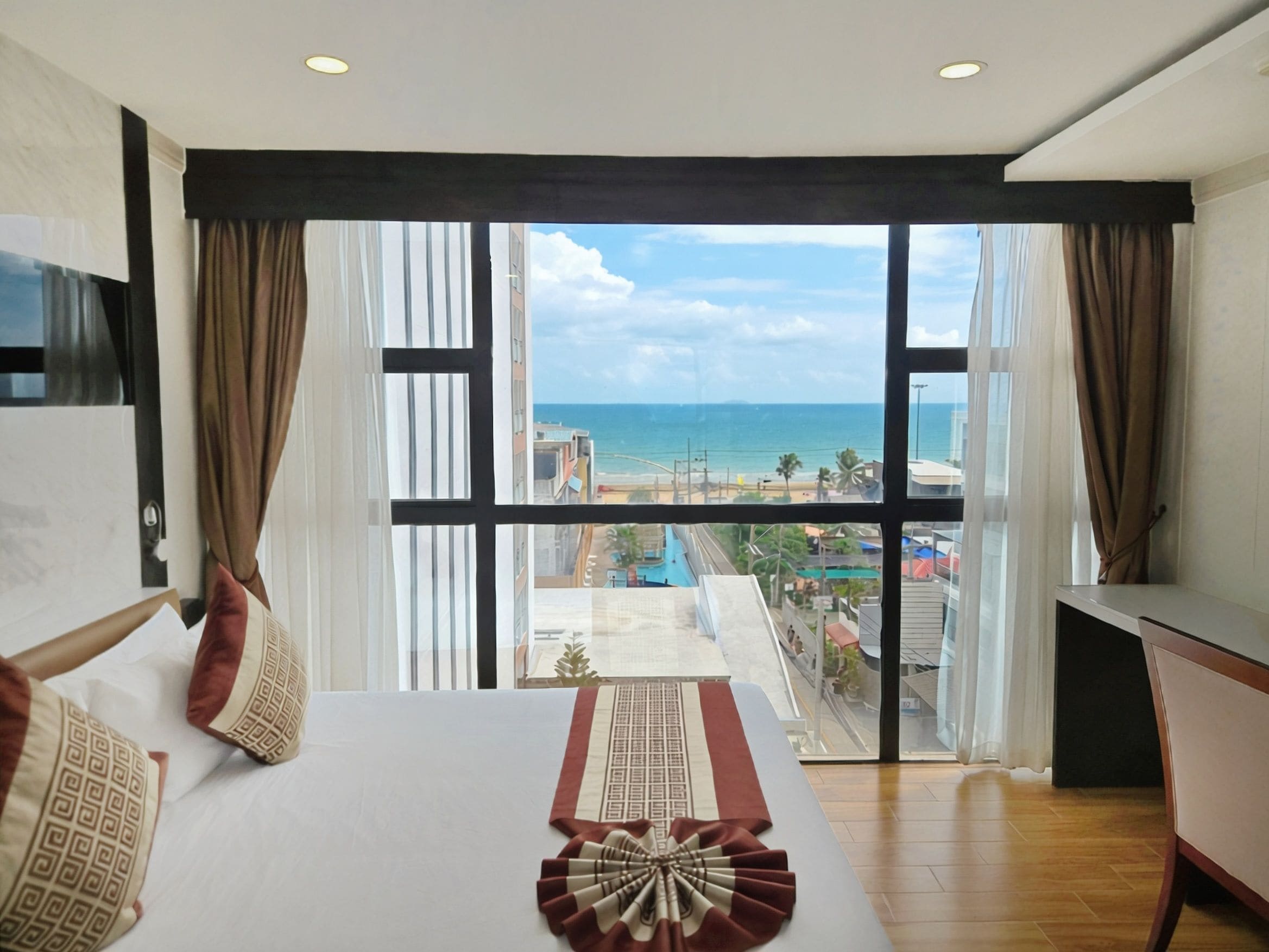 A hotel room with a large bed, a desk, and a view of the beach and cityscape.