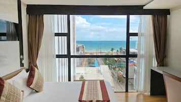 A hotel room with a large bed, a desk, and a view of the beach and cityscape.