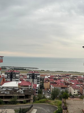 A residential area with multi-story buildings, a paved road, and a body of water in the background. - Erom Otel (Trabzon)