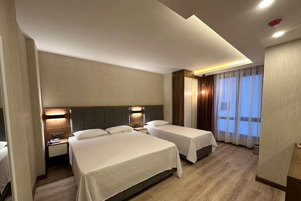 A hotel room with two beds, a nightstand, a lamp, and a large window with curtains.
