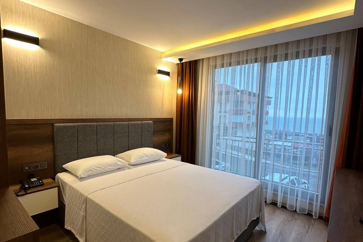 A hotel room with a large bed, a bedside table with a phone, and a window with curtains.