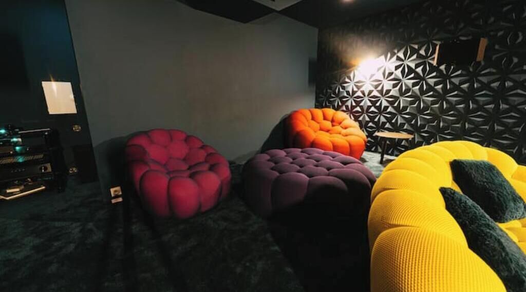 Une pièce comprenant quatre poufs colorés, à motifs et capitonnés, de couleur rouge, violette, orange et jaune.