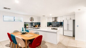 Una cucina moderna con mobili bianchi, un'isola centrale e un'area da pranzo con tavolo di legno e sedie colorate.