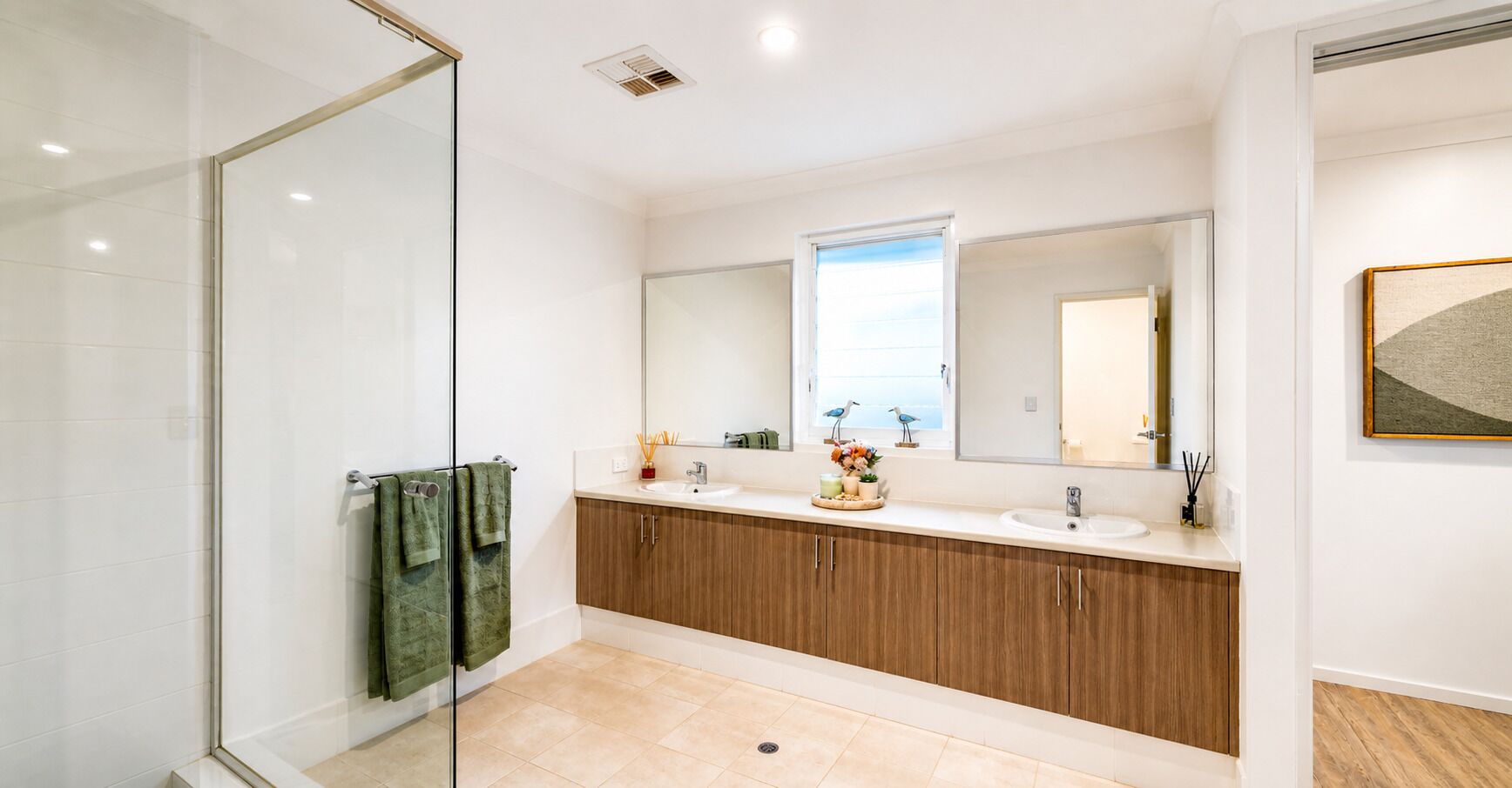 A modern bathroom with a glass shower enclosure, wooden cabinets, a large mirror, and a window with a view.