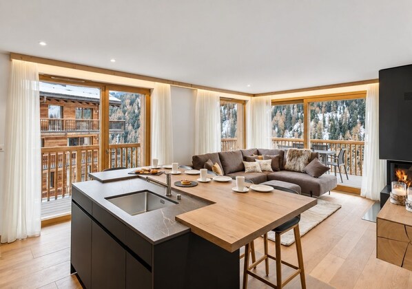 A modern kitchen with a central island, a dining area with a table and chairs, a sofa set, and a fireplace.