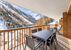 A balcony with a table and chairs, overlooking a snowy mountain landscape.