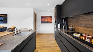 A modern kitchen with dark cabinetry, a wooden countertop, and a large island with a sink. - Luxury Apartment, 2 Bedrooms Rahas B Grimentz - By Mrs Miggins (Grimentz)