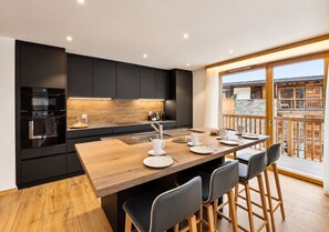 Eine moderne Küche mit einer Holztischinsel und Barhocker, einem Esstisch für vier Personen und einem Balkon mit Holzgeländer.