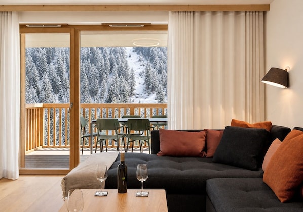 A modern living room with a sectional sofa, a wooden coffee table, and a view of a snowy forest through a sliding glass door.