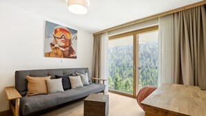 Una sala de estar moderna con un sofá gris, una mesa de centro de madera y un ventanal con vistas a un bosque.