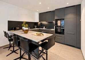 A modern kitchen with a central island, black chairs, and a vase of flowers.