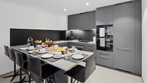 Una cocina moderna con comedor, que presenta una isla grande con alimentos para el desayuno, armarios grises y un horno empotrado.