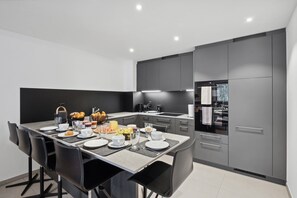 Una cucina moderna con zona pranzo, caratterizzata da un'isola grande con prodotti per la colazione, mobili da cucina grigi e forno integrato.