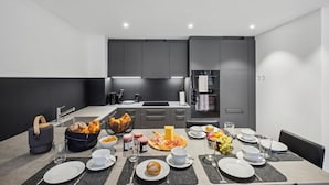 Una cocina moderna con armarios grises, un comedor listo para el desayuno con diferentes alimentos y bebidas, y un refrigerador al fondo.