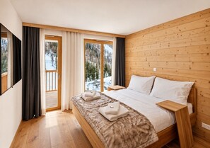 A bedroom with a large bed, wooden headboard, and a view of a snowy landscape through a sliding door.