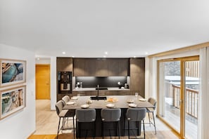 Een moderne keuken met donkere kastjes, een centraal eiland en een eethoek met zes stoelen en een tafel voor vier personen.