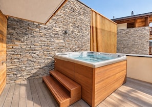 A hot tub on a wooden deck with stone walls.