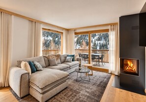 Ein modernes Wohnzimmer mit einer Eckcouch, einem Kamin und einem Balkon mit Blick auf Bäume.