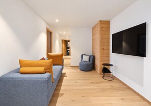 Ein modernes Wohnzimmer mit einer Couch, einem Sessel, einem Fernseher und einem kleinen Tisch.