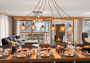 A cozy living room with a fireplace, dining area with breakfast setup, and a balcony with a view of trees.