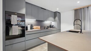 Uma cozinha moderna com armários cinzas, forno embutido, máquina de café e pia com torneira preta.