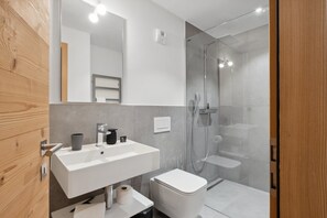 Casa de banho moderna com uma pia branca, sanita e cabine de duche com parede de vidro.