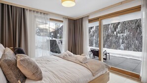 Quarto moderno com uma cama grande, vista para uma paisagem nevada através de uma porta de correr de vidro e uma atmosfera acolhedora.