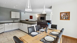 A modern kitchen with white cabinets, a dining area with a wooden table set for four, and a living area with a sofa and TV. - Beautiful apartment at The Lodge Champéry - By Mrs Miggins (Champéry)