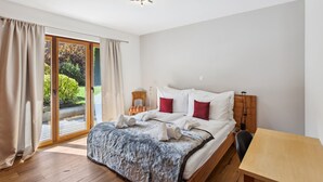 A bedroom with a wooden bed, a small table, and a view of a garden through a sliding glass door. - Beautiful apartment at The Lodge Champéry - By Mrs Miggins (Champéry)
