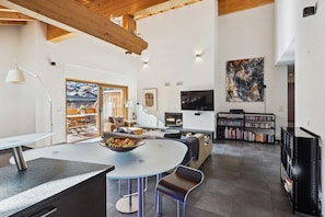 A modern living room with a round table, seating, a bookshelf, a TV, and a painting on the wall.
